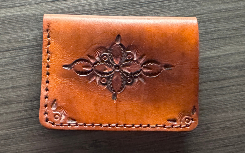 brown leather wallet stamped with a flower sits on a faux wood table.